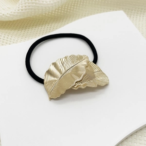Macro detail of golden metal leaf ornament with realistic veins on black elastic hair tie