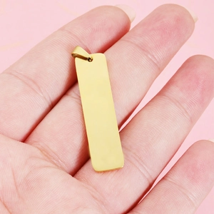 Golden rectangular stainless steel mirror pendant held in hand with soft pink background