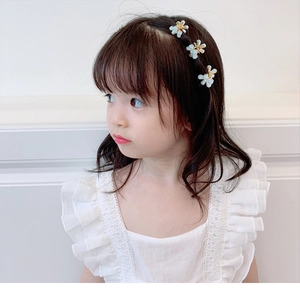 Détail de barrettes camélia avec perles et métal doré sur les cheveux d'une fille