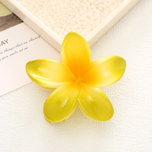 Macro view of a vibrant yellow plumeria shark hair claw clip on a white leather base