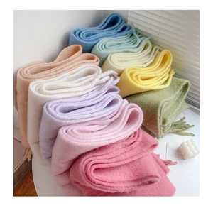 Detailed stack of soft plush winter scarves in various pastel colors with tassel edges