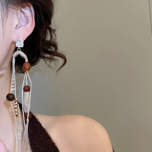 Macro shot of long fringe earrings with woven cords and amber beads worn by a model