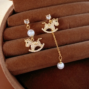 Macro detail of gold-plated rocking horse earrings with pearls and zircon stones