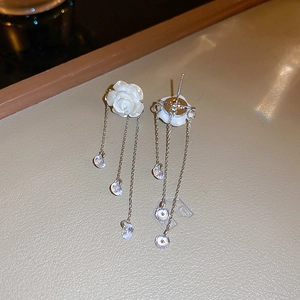 Détail de boucles d'oreilles camélia blanc avec glands en cristal sur fond de cuir