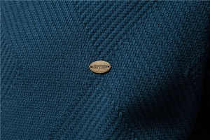 Detail of navy knit fabric with premium bronze oval metal brand tag from a slim cardigan