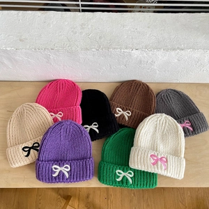 Flat lay of warm knitted baby beanies in eight colors with cute bow embroidery details
