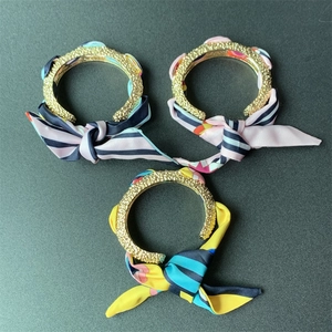 Detail of matte gold open bangles wrapped with various printed floral silk ribbons