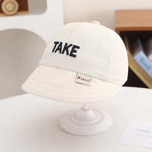 Close-up of beige cotton kids baseball cap featuring black TAKE embroidery and KUKUJI label