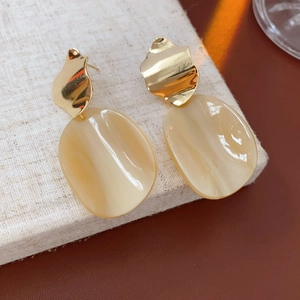 Détail de boucles d'oreilles ovales en acrylique avec clous dorés sur fond en cuir brun