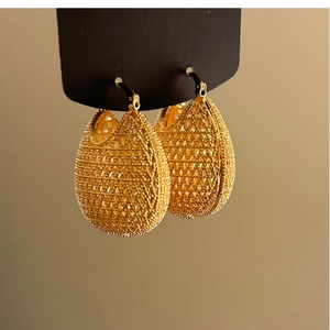 Vintage gold teardrop earrings with geometric hollow weave pattern on sand background