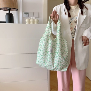 Dettaglio della borsa shopping in tela con motivo floreale verde indossata dal modello