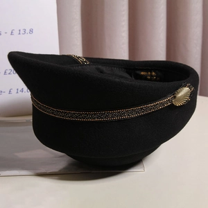 Detailed macro view of black wool beret featuring gold woven band and shell buckle