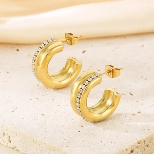 Close-up of golden C-shaped earrings with micro-paved white rhinestones on silk