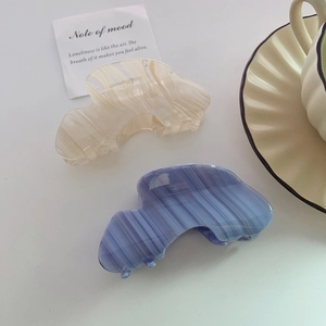 Elegant acetate hair claws in beige marble and blue striped pattern on a white surface