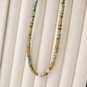 Ethnic style necklace with green beaded stones and gold metal accents on jewelry box