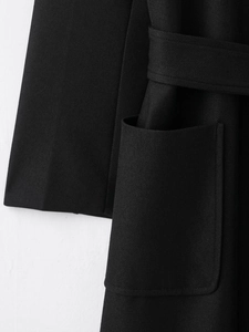 Detail of black wool blend coat cuff, side pocket and twill texture on a white background