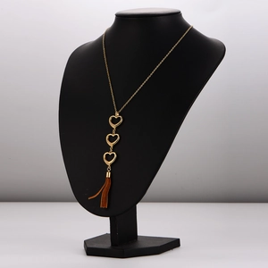 Gold stainless steel heart necklace with rhinestones and brown tassels on a black display