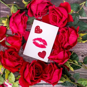 Close-up of heart stickers and lip prints on cards surrounded by red roses on wood