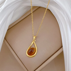 Detail of a golden water-drop pendant with oval amber stone on a beige jewelry box