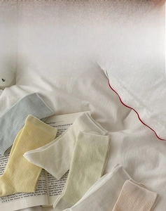 Detailed close-up of ribbed cotton crew socks in pastel colors on a soft white bed