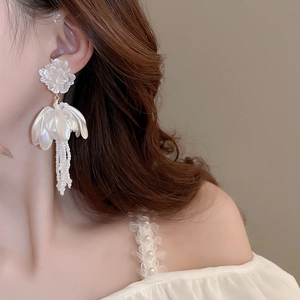 Detail of elegant white petal tassel earrings with faux pearls worn by a model