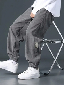 Detail of grey corduroy joggers showing embroidery patches and ribbed cuffs on model