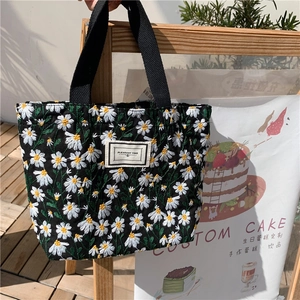 Detail of embroidered daisy patterns and fabric label on black canvas tote bag
