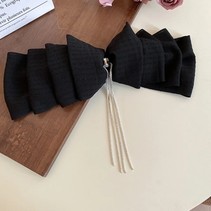 Detailed close-up of a black lace bow hair clip with silver rhinestone tassels on dark wood