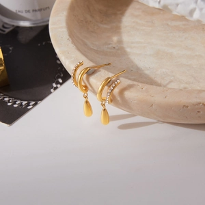 Détail de boucles d'oreilles créoles C dorées avec zircon et pendentif goutte d'eau