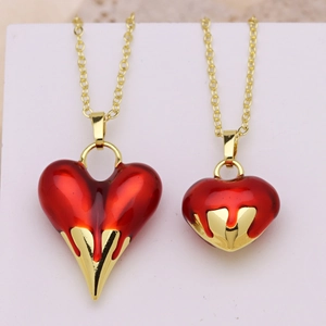 Gold plated chain necklace with vibrant red heart pendant over a soft pink background