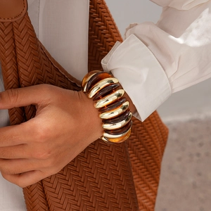 Detail of wide acrylic amber and gold metal elastic bracelet worn with elegant outfit
