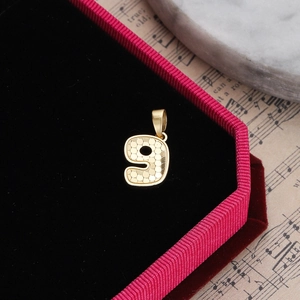 Golden number 9 pendant with honeycomb texture in a velvet jewelry box on sheet music