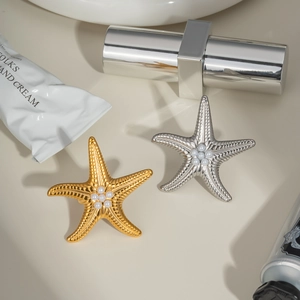 Detailed view of starfish rings with pearls in gold and silver finishes on a beige background