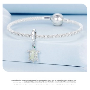Detailed close-up of a silver mesh bracelet featuring a luminous turtle charm with green stones