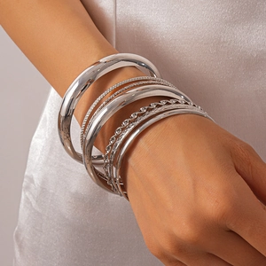 Close-up of a diverse 8-piece silver metal bangle set worn on a model's wrist over white satin