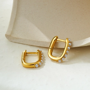 Minimalist 18K gold U-shaped earrings with faux pearl inlay on a beige textured background
