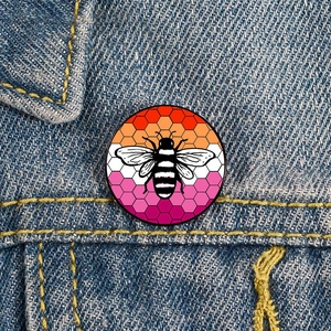 Rainbow bee enamel pin with honeycomb pattern on a blue denim jacket pocket