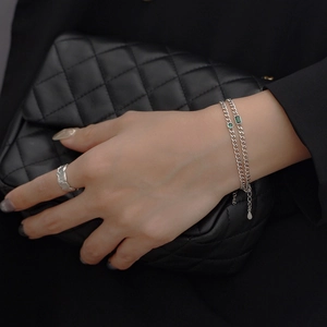 Detail of silver tank chain bracelet with green gemstones on black quilted background