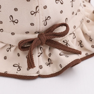 Gros plan d'un chapeau bob pour bébé beige avec nœud marron et texture imprimé floral