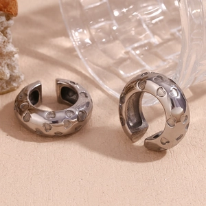 Detailed view of silver heart-patterned ear cuffs on a rock and glass background