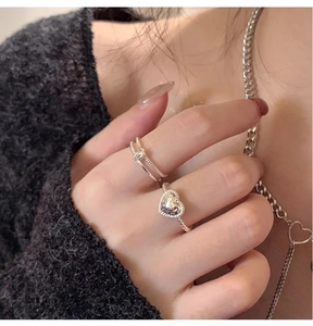 Close-up of minimalist silver heart ring and twisted rope band worn on a black knit