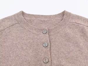 Close-up of ribbed crewneck and dark buttons on a textured gray knit cardigan