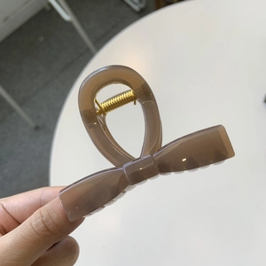 Detail of coffee brown bow hair claw clip with glossy finish and gold metal spring