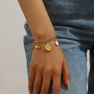 Bracelet doré avec breloques océaniques, coquillages blancs et hippocampe sur jean