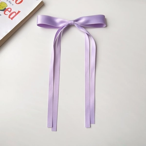 Detailed close-up of a purple satin ribbon bow hair clip on a clean aesthetic background