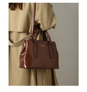 Detailed view of glossy brown leather tote bag with Fashion & Bags text on beige coat