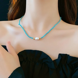 Close-up of model wearing turquoise and freshwater pearl necklace with gold accents