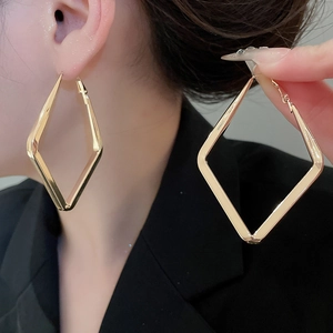 Close-up of elegant gold rhombus pendant earrings with smooth metallic finish on model
