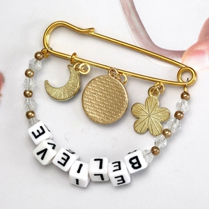 Golden brooch pin featuring celestial moon charms and a Believe lettered bead strand