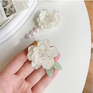 Dettaglio macro del fermaglio a camelia con perle e foglie verdi su vassoio bianco